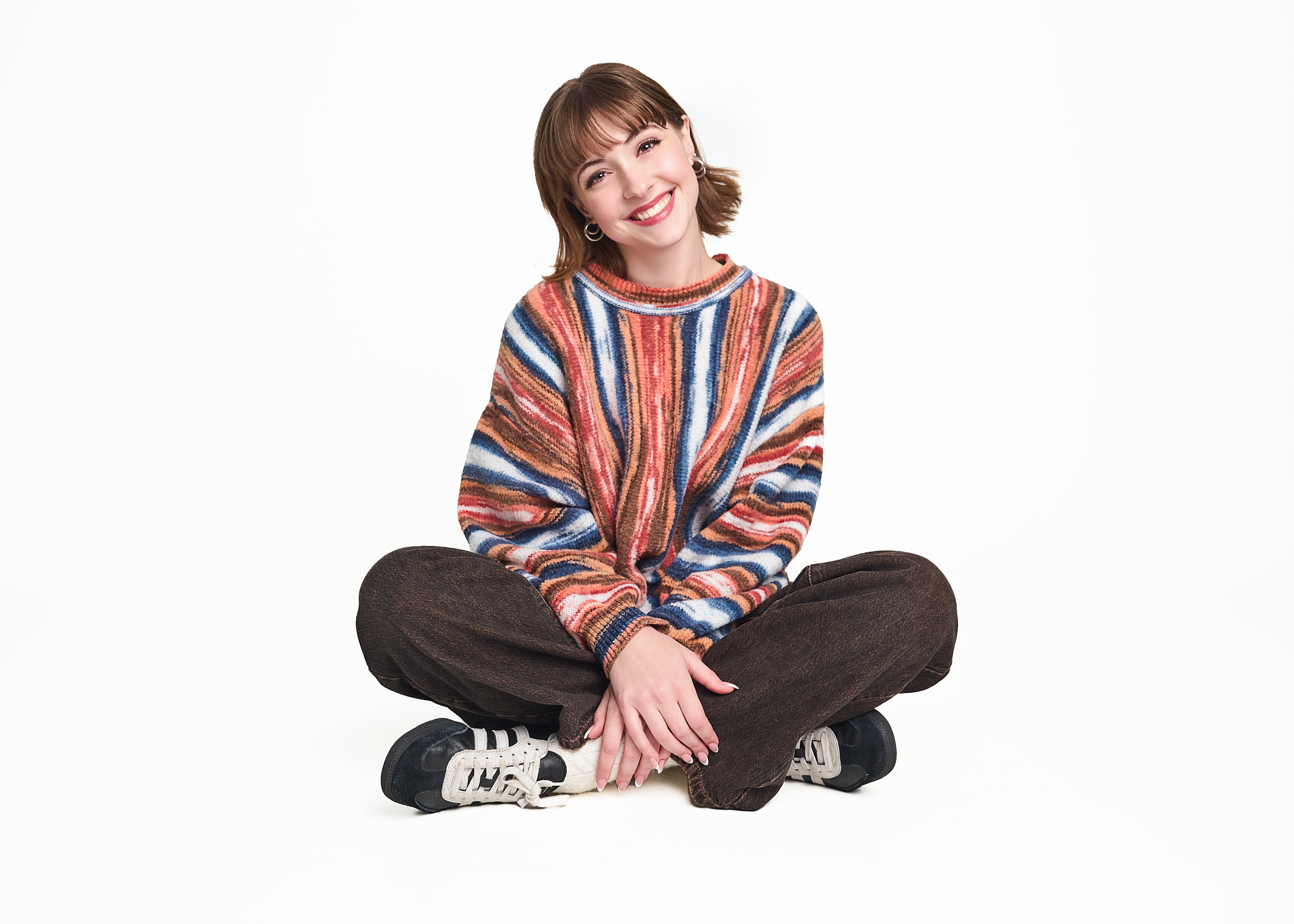 high school senior sitting on a white background wearing fashion forward sweater.