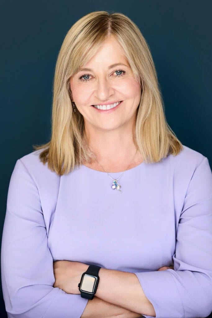 Professional headshot of blonde woman in lavender top with arms crossed against teal background Minnesota Megan Engeseth Photography