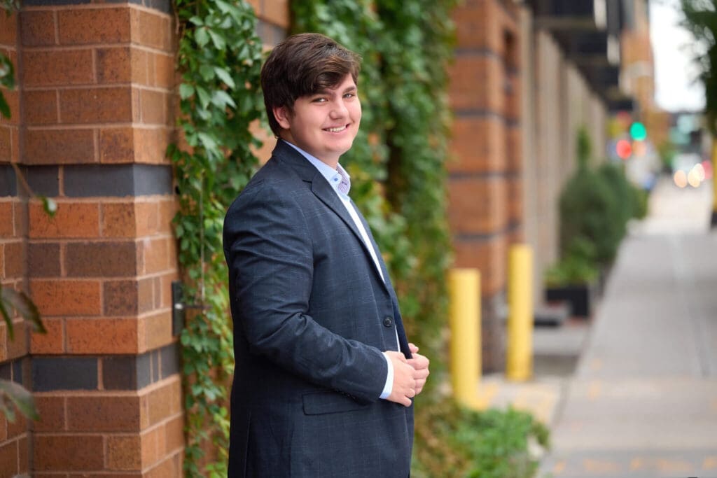Senior picture for Woodbury High School guy with suit and ivy and brick with a big smile